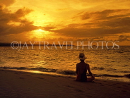 DOMINICAN REPUBLIC, North Coast, Playa Dorada, tourist seated on beach, watching sunset, DR334JPL